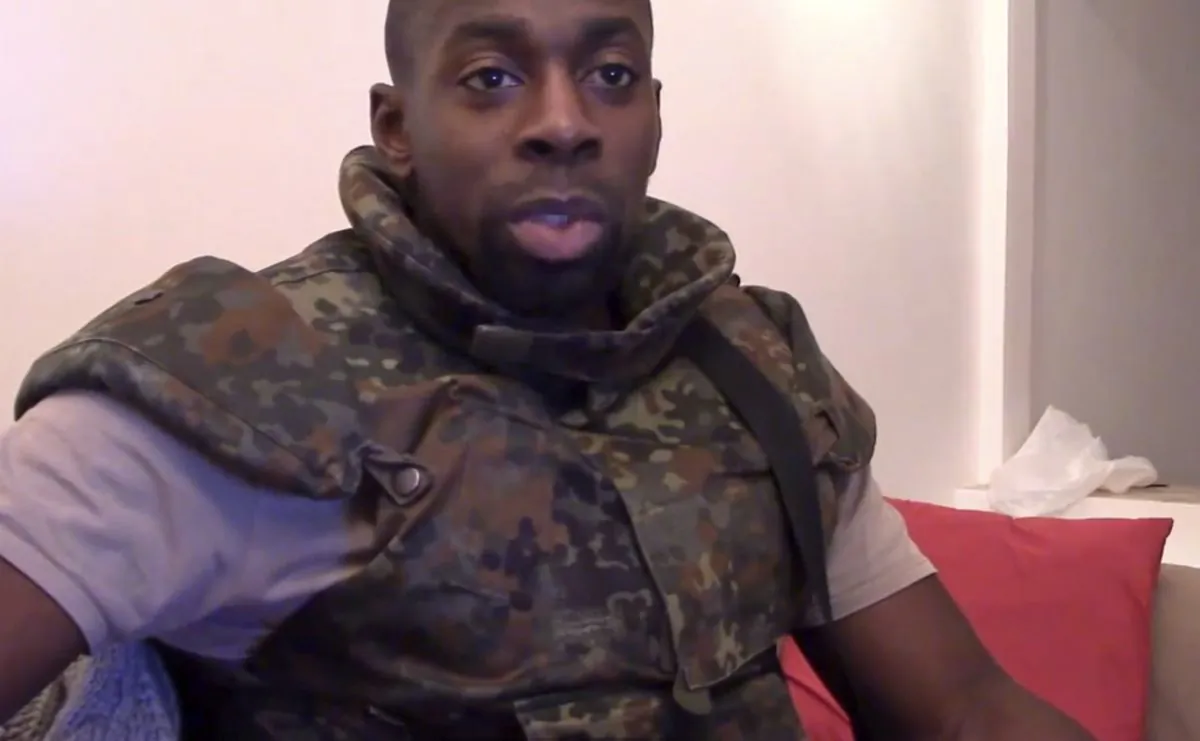 This image mahostage-taker Amedy Coulibaly, who shot a policewoman and four hostages at a kosher grocery in Paris, speaking in broken Arabic that he seems to be reading from a paper, in front of an Islamic State emblem, as he defends the attacks carried out on the satirical newspaper Charlie Hebdo, police and the Jewish store. At one point, Coulibaly says Charlie Hebdo will be attacked "tomorrow" and that he and the (Said and Cherif Kouachi) brothers were coordinating. (AP Photo/Militant Video)