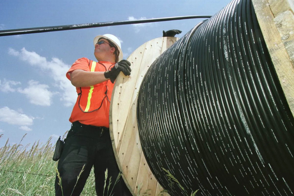 Reeltender Mo Laussie watches fiber-optic cable as he helps install the cable unto telephone poles June 21, 2001 in Louisville, CO. (Photo by Michael Smith/Getty Images)
