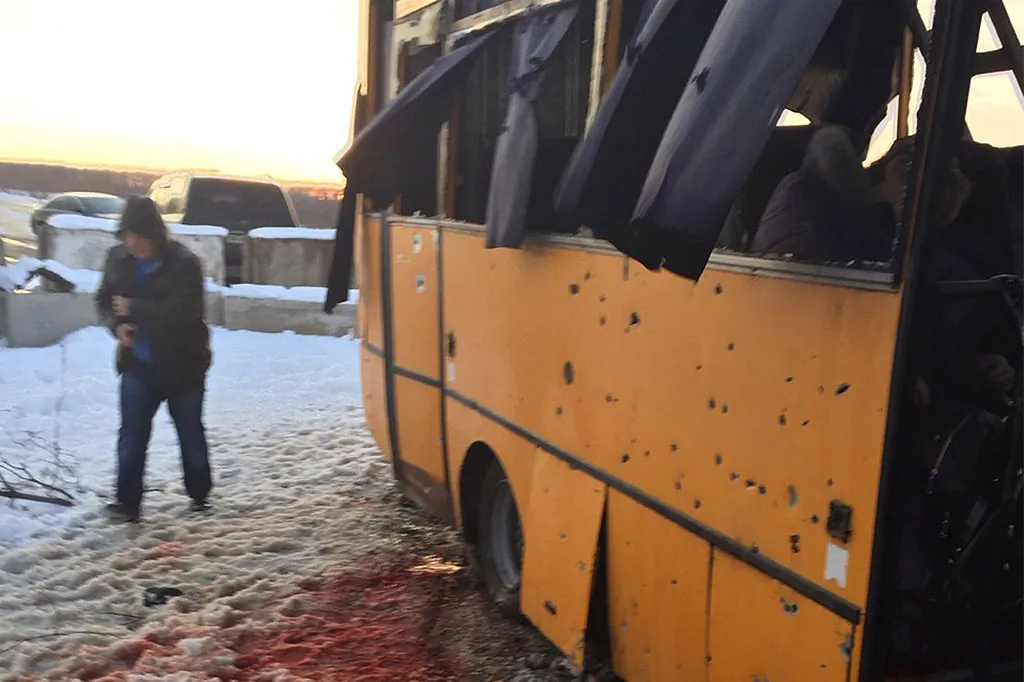 A man walks past snow covered with blood as he passes by a bus destroyed by a rebel shell at the checkpoint near the town of Volnovakha in the Donetsk region, eastern Ukraine, Tuesday, Jan. 13, 2015. At least 12 civilians were killed and others wounded as the bus was hit by a pro-Russia separatists' shell while passing through the checkpoint, local officials said. (AP Photo/Ukrainian Interior Ministry)