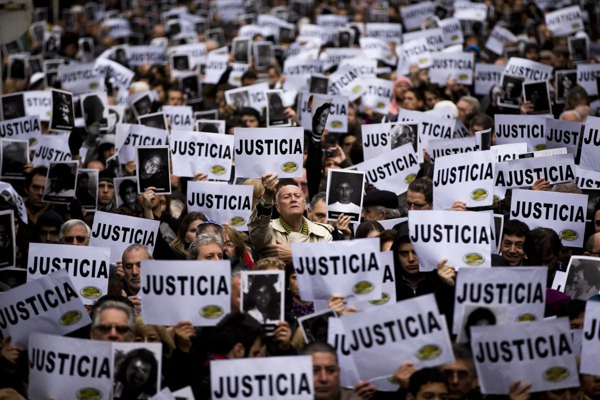 People hold up signs that read in Spanish: "Justice" and pictures of the victims of the bombing of the Argentine-Israeli Mutual Association community center on the 19th anniversary of the terrorist attack, in Buenos Aires, Argentina, on July 18, 2013. In a statement released Wednesday, Jan. 14, 2015, Argentine Prosecutor Alberto Nisman, who is investigating the 1994 bombing of the Jewish community center, accused President Cristina Fernandez of reaching a deal with Iran to avoid punishing those responsible. (AP Photo/Victor R. Caivano)