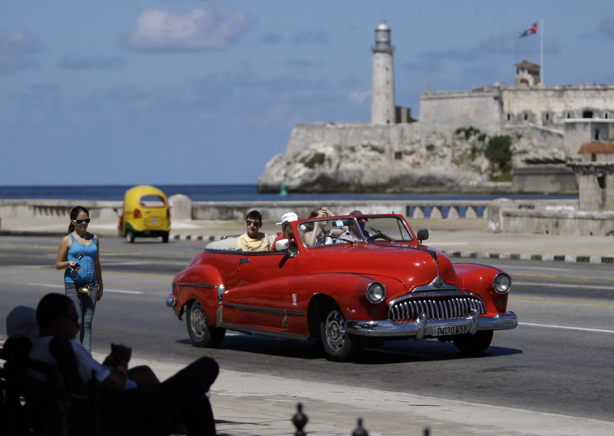 In this Oct 12, 2013 photo, tourists ride in a classic American car on the Malecon in Havana, Cuba. A new set of U.S. government regulations takes effect Friday, Jan. 16, 2015, severely loosening the 50-decade long travel and trade restrictions for Cuba. (AP Photo/Franklin Reyes)