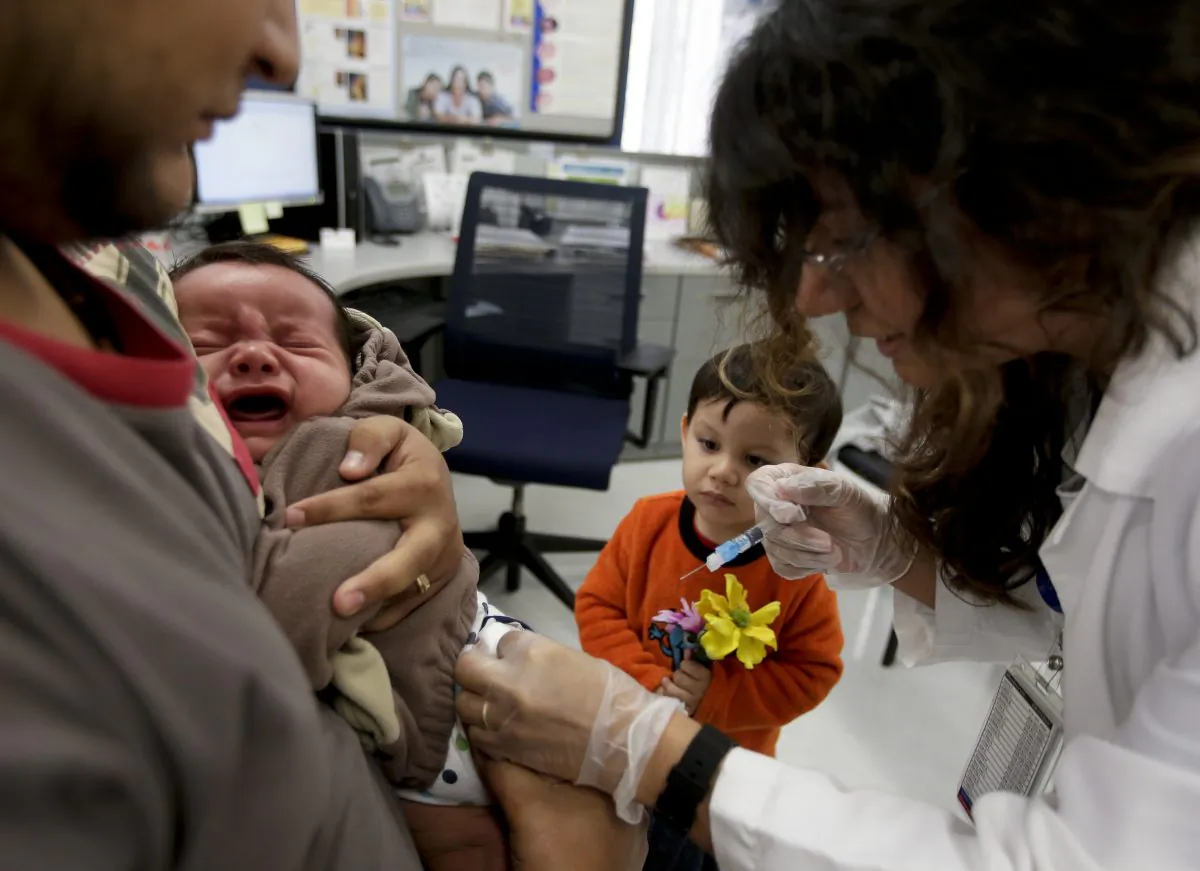 Julietta Losoyo (R), a registered nurse at the San Diego Public Health Center, gives Derek Lucero a whooping cough injection while in his father Leonel's arms as his brother Iker, 2, looks on, on Dec. 10, 2014. (AP Photo/Chris Carlson)