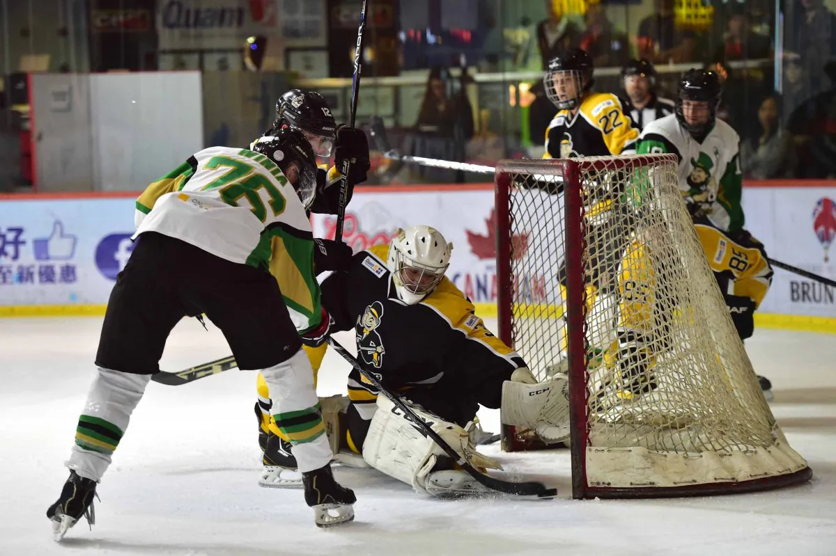 Darren Winia of the Macau Aces slots the puck into goal avoiding the clutching hand of Hong Kong Tycoons’ King Ho in their CIHL match at Mega Ice on Saturday Jan 17, 2015. Aces won the contest with a massive 13-4 score line. (Bill Cox/Epoch Times)