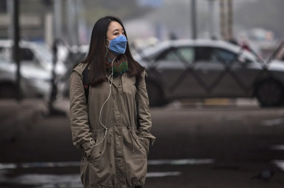 A foreign tourist wears a mask to protect herself from pollutants while walking on a sideway in New Delhi, India on, Jan. 23, 2015. Hazy skies served as the backdrop to meetings with Indian Prime Minister Narendra Modi and other officials who discussed India's biggest environmental woes. (AP Photo/Tsering Topgyal)