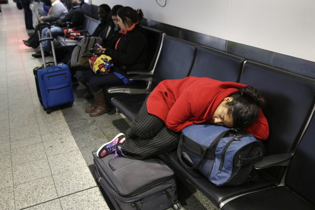 A woman sleeps on top of her luggage at LaGuardia Airport in New York, Monday, Jan. 26, 2015. Airlines canceled thousands of flights into and out of East Coast airports as a major snowstorm packing up to 3 feet of snow barrels down on the region. (AP Photo/Seth Wenig)