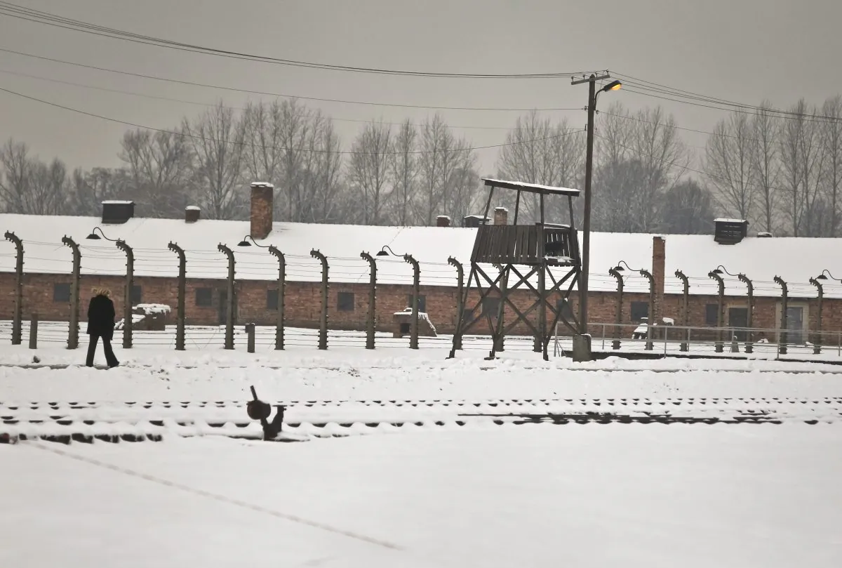 A woman walks by barbed wire fences surrounding detention buildings at the Birkenau Nazi death camp in Oswiecim, Poland, Monday, Jan. 26, 2015. (AP Photo/Czarek Sokolowski)