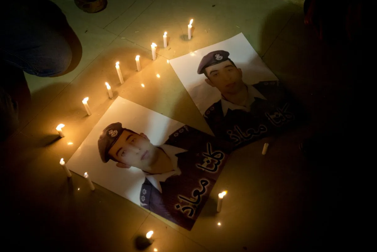 Members of Al-Kaseasbeh, the tribe of Jordanian pilot, Lt. Muath al-Kaseasbeh, who is was murdered by the Islamic State group militants, light candles by posters with his picture and Arabic that reads "we are all Muath." (AP Photo/Nasser Nasser)