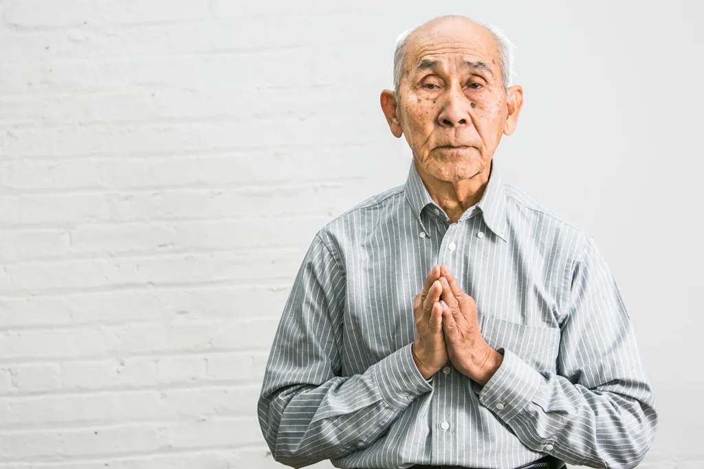 Khmer Rouge survivor Nal Oum performs "Sampeah," the Cambodian greeting or a way of showing respect, in New York, on Jan. 23, 2015. (Benjamin Chasteen/Epoch Times)
