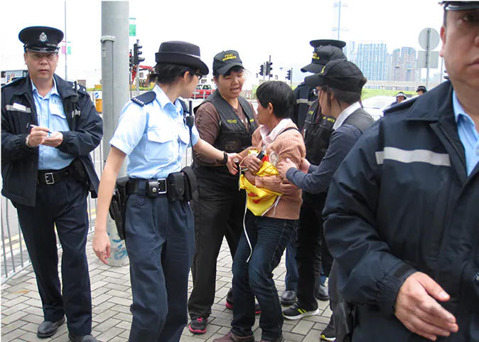 Food and Environmental Hygiene Department officers are attempting to take away a Falun Gong banner held by a practitioner Ms Poon (center) on May 2, 2013. (Epoch Times)