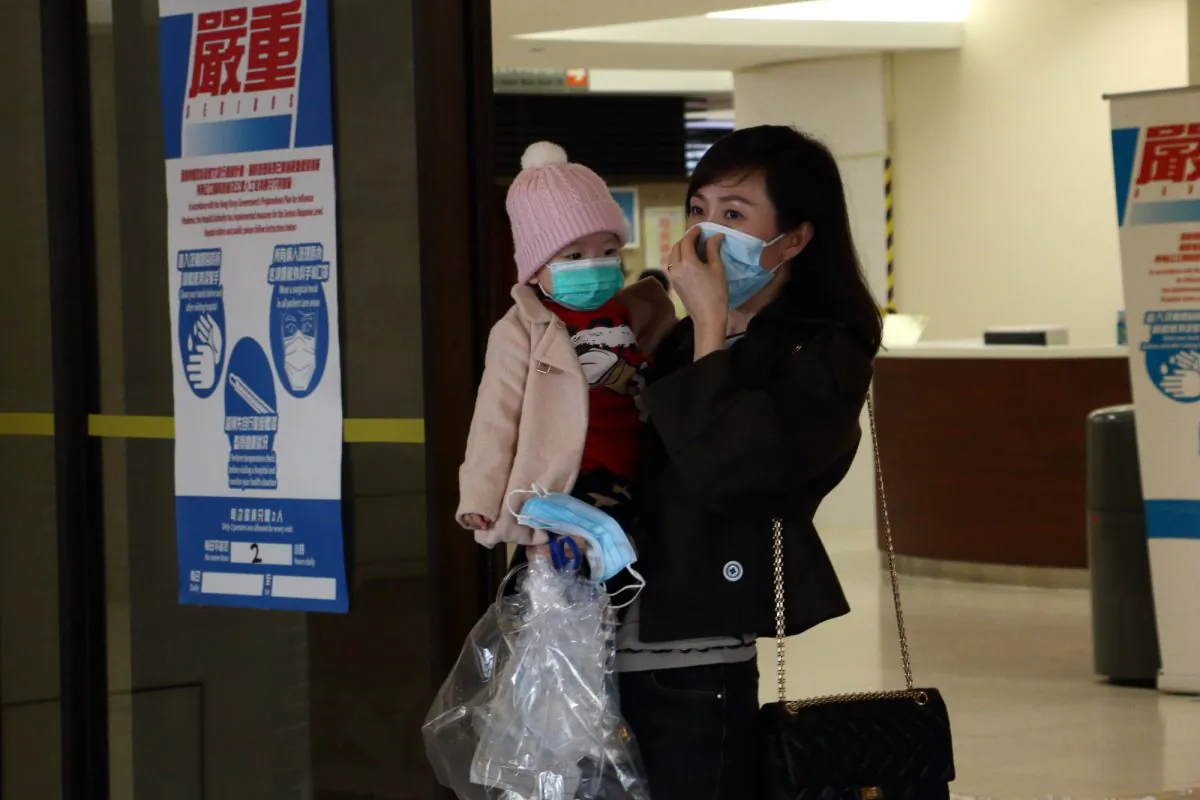 A woman holds a child while putting on a mask at Queen Mary Hospital on Feb. 5. (Kiri Choi/Epoch Times)