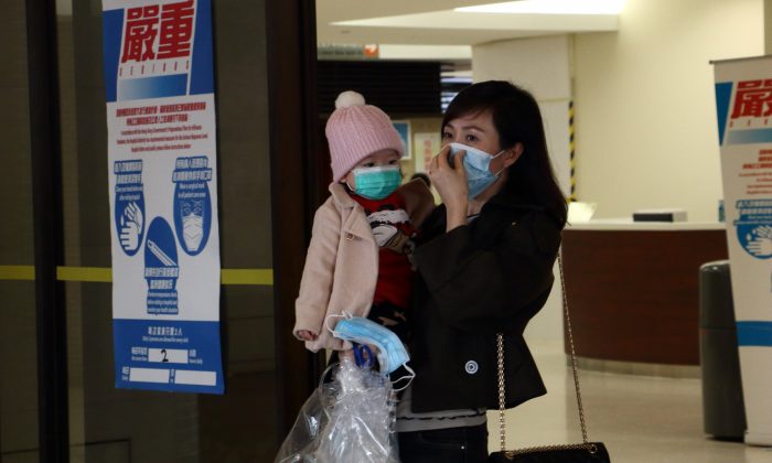 A woman holds a child while putting on a mask at Queen Mary Hospital on Feb. 5. (Kiri Choi/Epoch Times) 