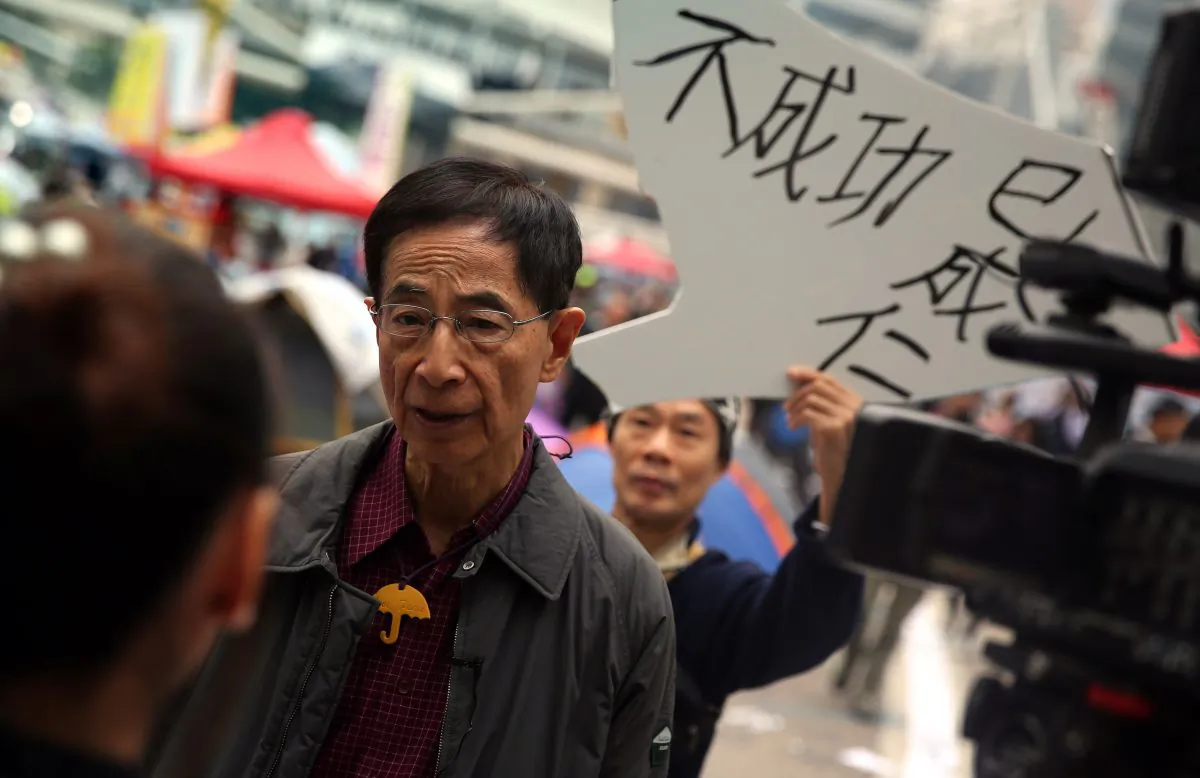 Martin Lee (2nd L), the founding chairman of the Democratic Party in Hong Kong, is interviewed by the media while a protester (behind) holds up a sign of support at the main pro-democracy protest site in the Admiralty district of Hong Kong on Dec. 11, 2014. (Isaac Lawrence/AFP/Getty Images)