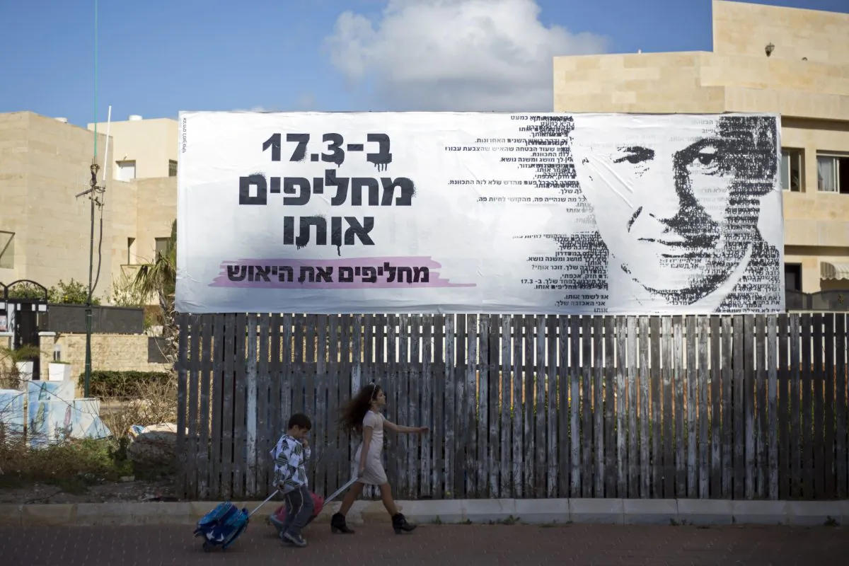Children pass by an election campaign banner with a painting of Israel's Prime Minister Benjamin Netanyahu, in Netanya, Israel, Monday, March 2, 2015. (AP Photo/Ariel Schalit)