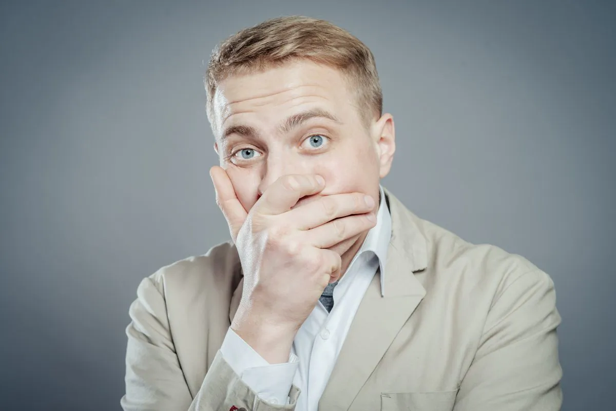 Businessman covers mouth with hand. (Shutterstock*)