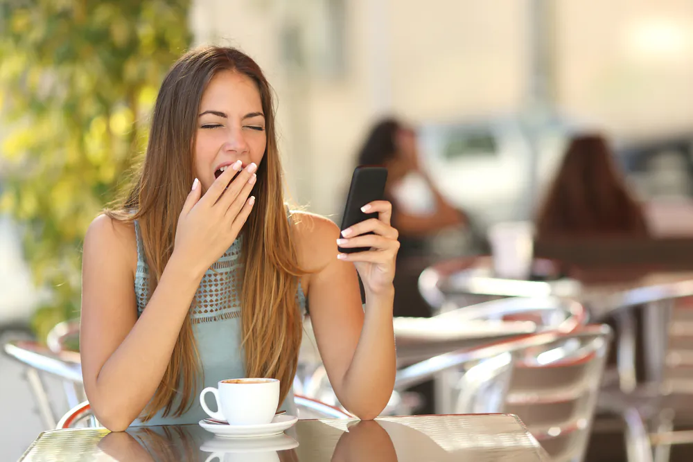 Tired woman yawning while working on phone. (Shutterstock*)