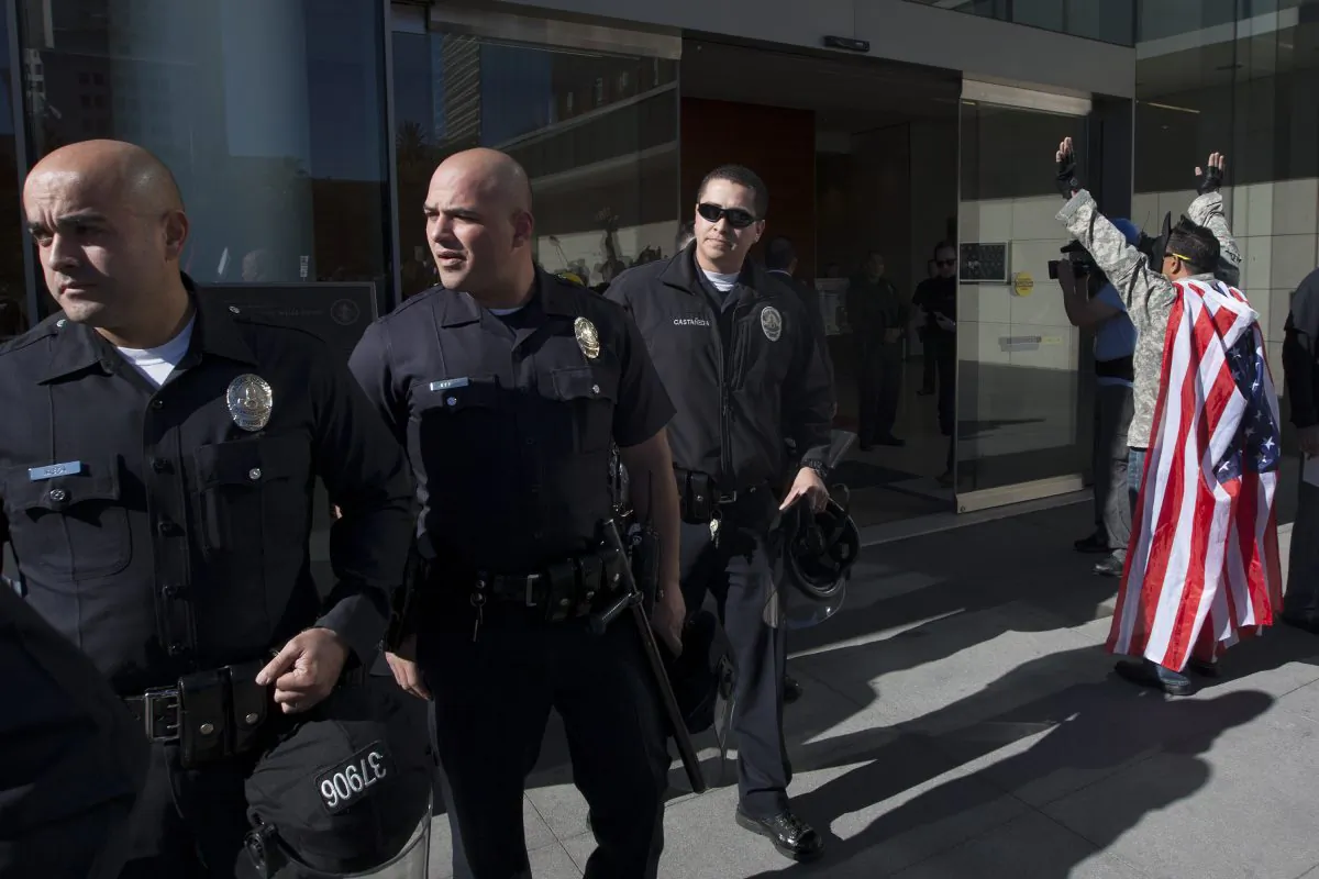 Police officers pass a man with a flag for a cape as protesters at Los Angeles Police Department Headquarters rally to express their anger over the fatal police shooting of an unarmed homeless man on March 3, 2015 in Los Angeles, California. (Photo by David McNew/Getty Images)
