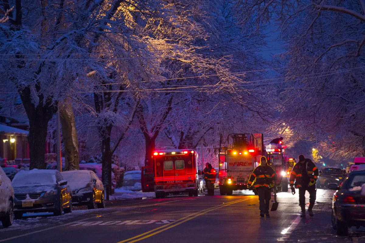 Firefighters walk near the scene of a fire, center left, in which seven children died in the Brooklyn borough of New York, March 21, 2015. (AP Photo/Craig Ruttle)