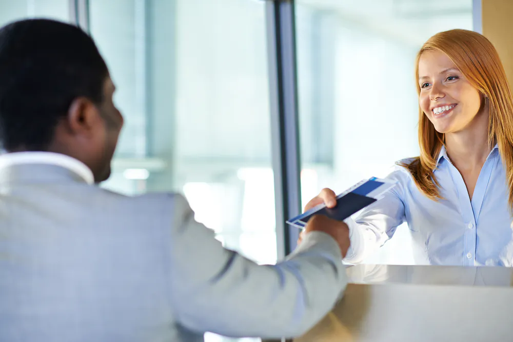 A young woman giving passport and ticket back to businessman at airport check-in counter via Shutterstock*