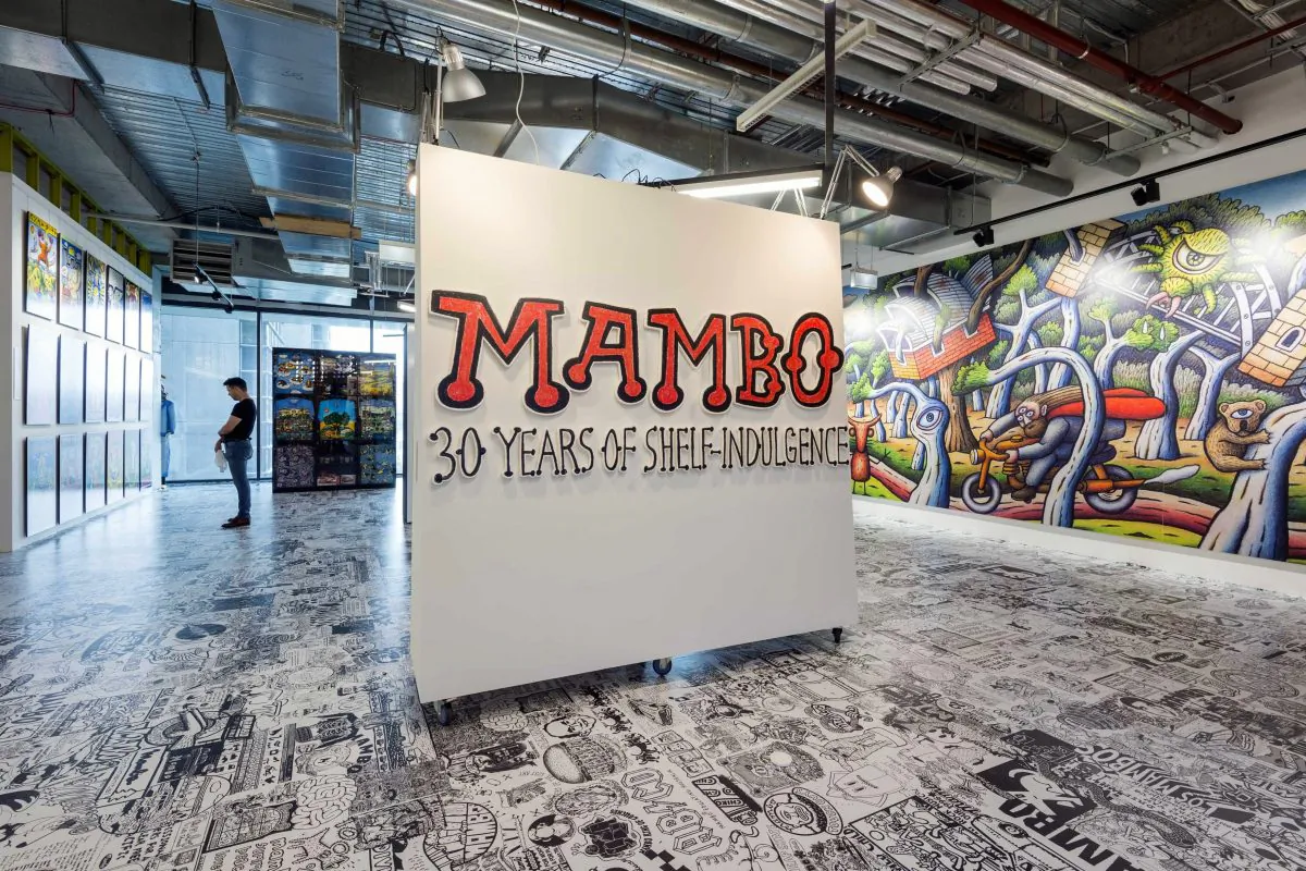 The entrance to the Mambo exhibition at aMBUSH GALLERY. In the background is part of the "Millennial Wallscape" a Reg Mombassa mural commissioned to celebrate the recent 40th anniversary of the Sydney Opera House. It was painted on a construction hoarding for a building site in the Opera House's southern forecourt. (Courtesy of aMBUSH Gallery) 