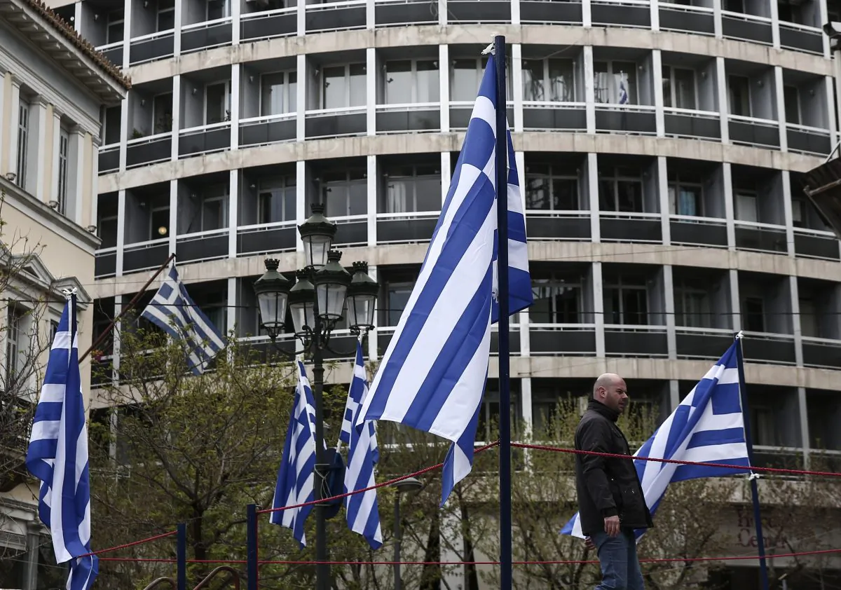 A municipal worker walks between Greek flags in Athens, on April 9, 2015. (AP Photo/Yorgos Karahalis)