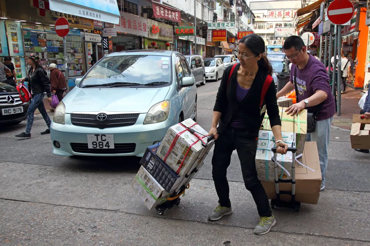 Two mainlanders carry their goods on trolleys walking across street at Sheung Shui, Northern District of Hong Kong on April 12, 2015. (Epoch Times)