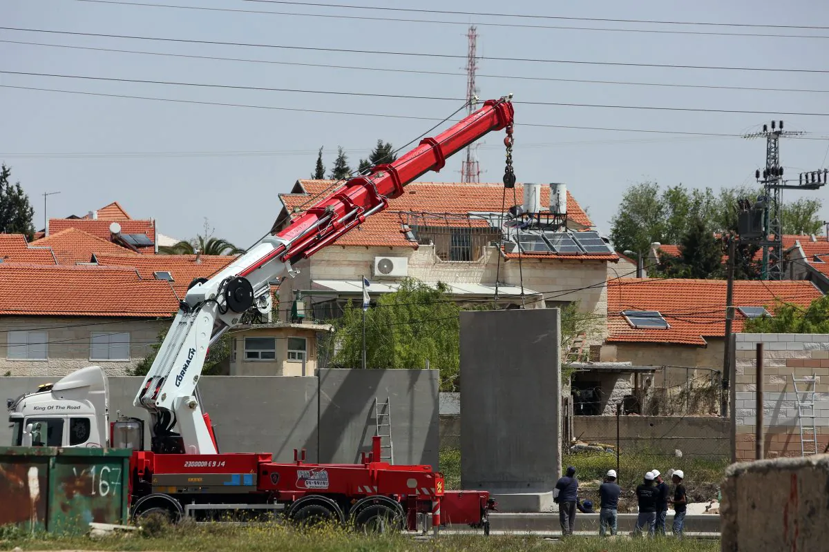 An Israeli crane lifts a section of concrete as they build a defensive wall around the Israeli settlement of Beit El, in the occupied West Bank north of Ramallah on April 7, 2015, next to a road used by Palestinians from the adjacent Jalazon refugee camp. (Abbas Momani/AFP/Getty Images)
