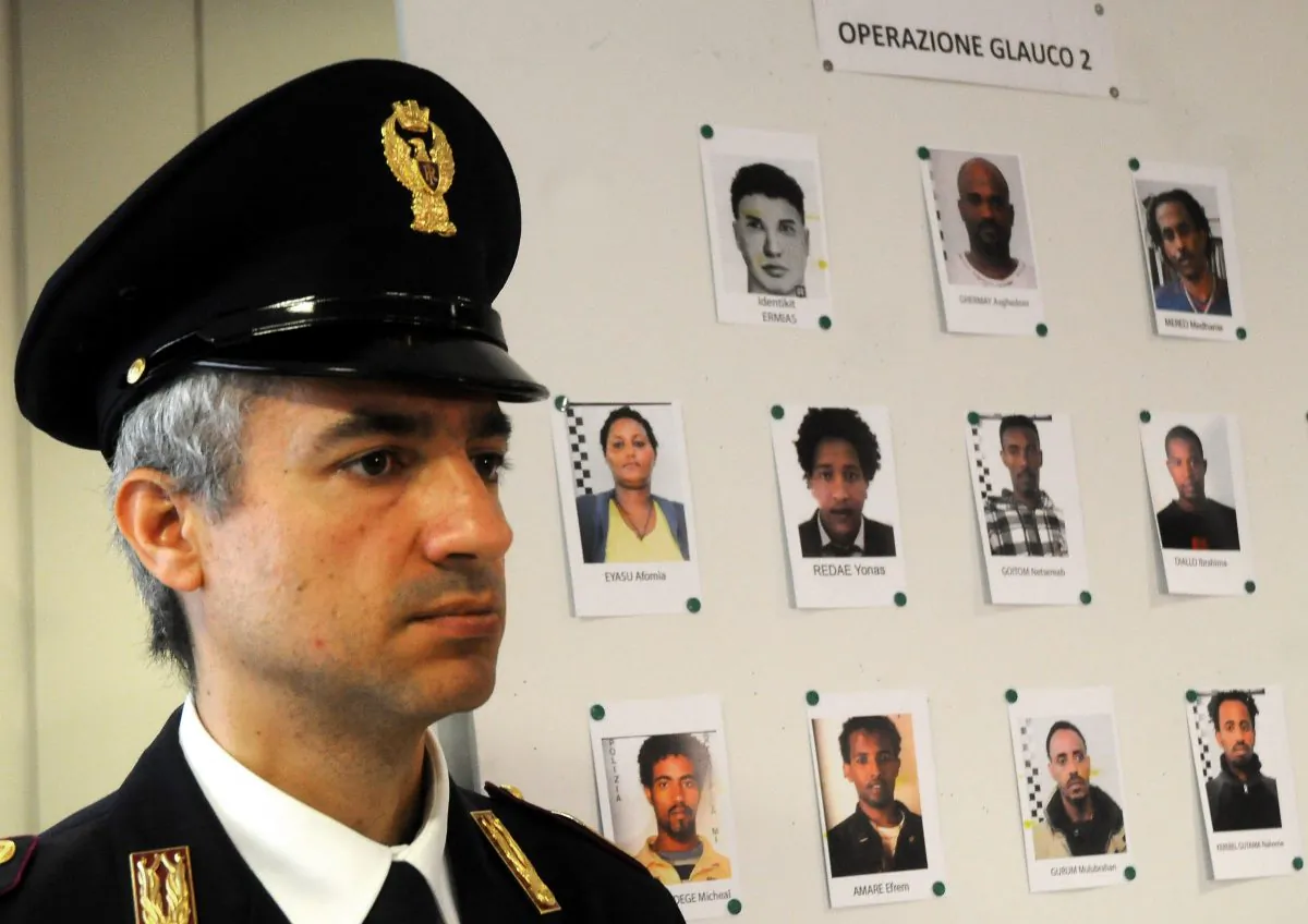 An Italian Police officer stands next to mug shots of alleged migrant traffickers shown during a press conference, in Palermo, Sicily, Italy, Monday, April 20, 2015.(AP Photo/Alessandro Fucarini)