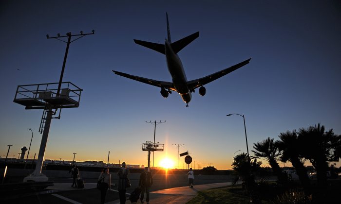 Passengers pull their luggage outside Los Angeles International Airport (LAX) as a plane comes in for a landing at dusk in Los Angeles on Nov. 1, 2013. (Robyn BeckAFP/Getty Images)
