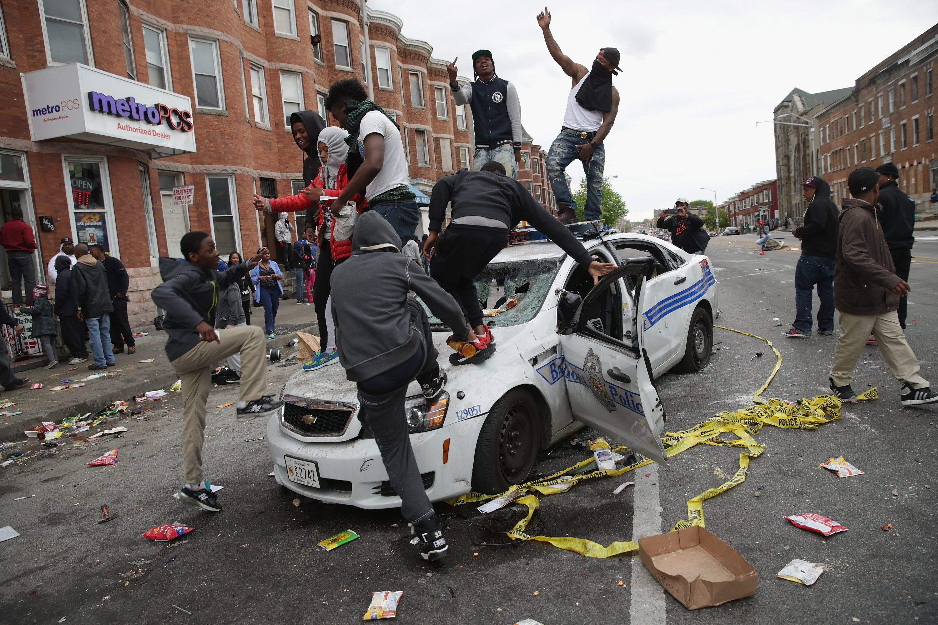 Demonstrators climb on a destroyed Baltimore Police car in the street near ...