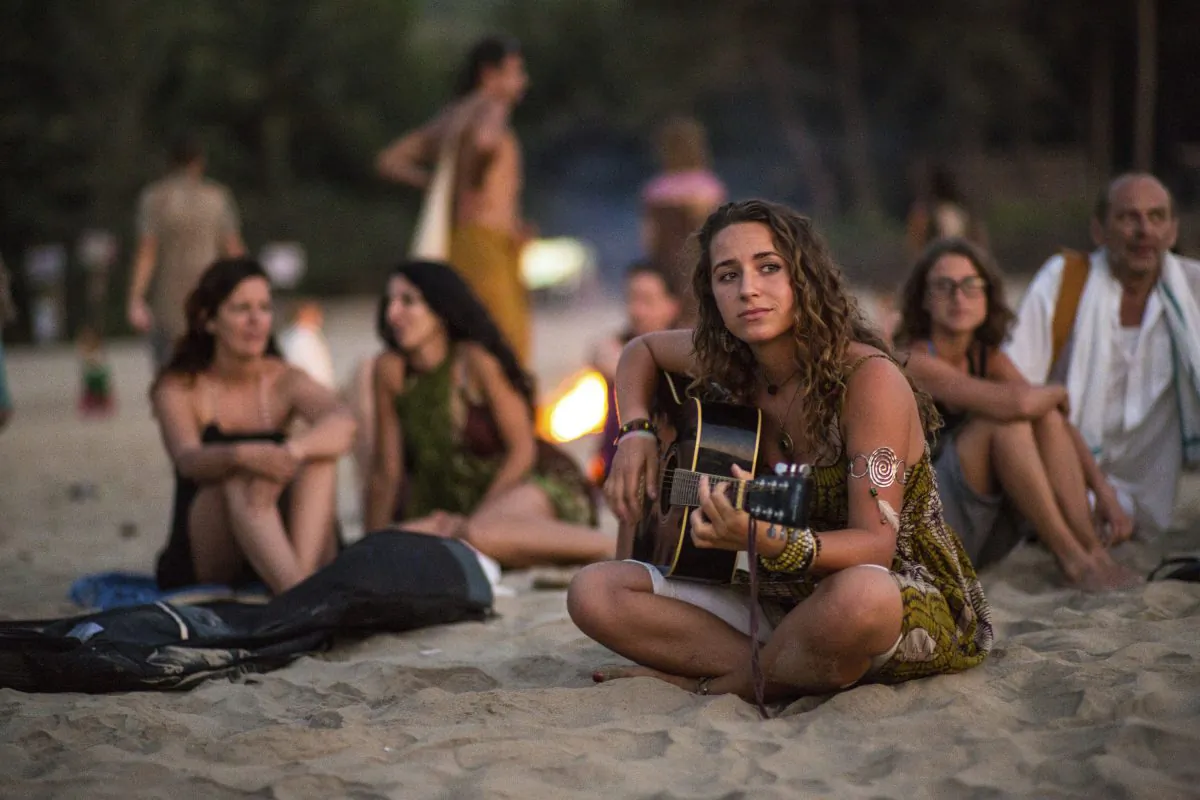As the sunsets a woman plays guitar as people behind her gather around a bond fire on the Gokarna beach in India. (Jedraszak/iStock)
