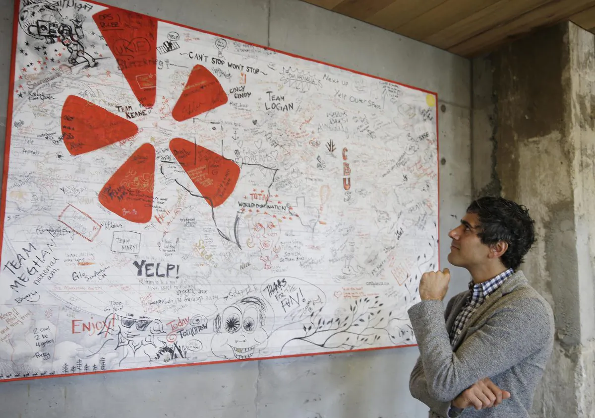 In this photo taken Friday, Aug. 1, 2014, Yelp CEO Jeremy Stoppelman looks over a wall signed by visiting employees from other cities at his company's headquarters in San Francisco. (AP Photo/Eric Risberg)