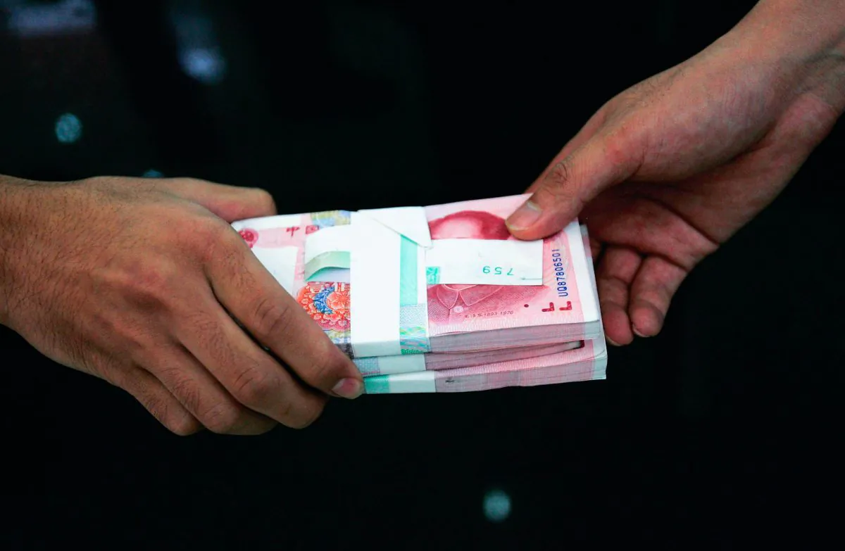 A clerk passes on stacks of Chinese yuan to another clerk at a bank in Beijing, China on July 22, 2005. (China Photos/Getty Images)