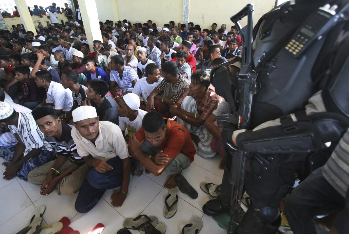 An armed police officer stands guard as ethnic Rohingya men gather upon arrival at a temporary shelter in Lhoksukon, Indonesia, on May 13, 2015. (Binsar Bakkara/AP Photo)