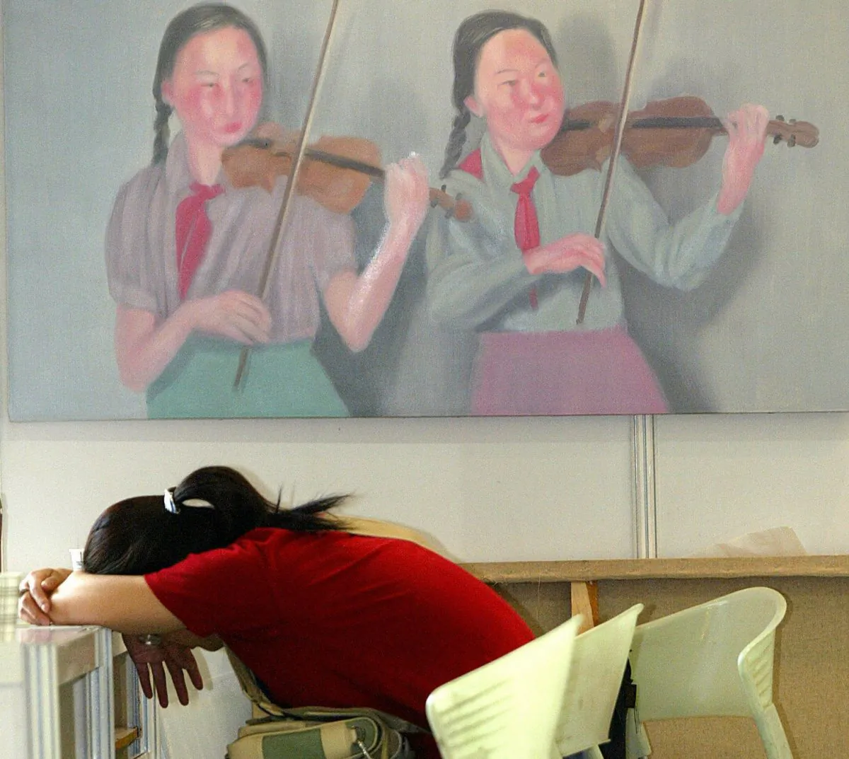 A woman takes a nap before an oil painting featuring two young pioneers playing violins at the Shanghai Spring Art Salon, 03 June 2004. (LIU JIN/AFP/Getty Images)