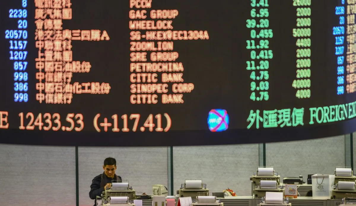 A trader walks the floor of the Hong Kong Stock Exchange as share prices are flashed above on Jan. 2, 2013. Two Hong Kong-listed companies recently lost over 40 percent of their value within a day. (Antony Dickson/AFP/Getty Images)
