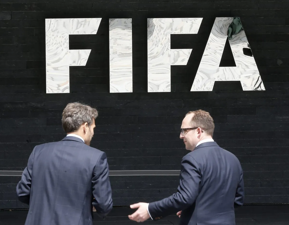 Two men talk to each other in front of the FIFA logo at the FIFA headquarters in Zurich, Switzerland, on May 27, 2015. (AP Photo/Michael Probst)