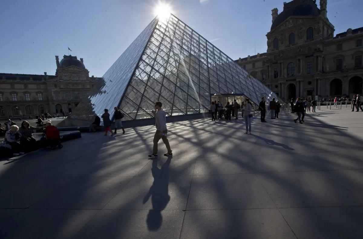 A man passing by the glass-pyramid of the Louvre museum in Paris, France on Oct. 14, 2014. (Michel Euler/File via AP)