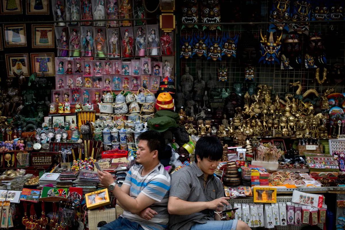 Vendors browse their smartphones as they wait for customer at their store selling Chinese made souvenirs at the Wangfujing shopping district in Beijing on May 21, 2015. (Andy Wong/AP)
