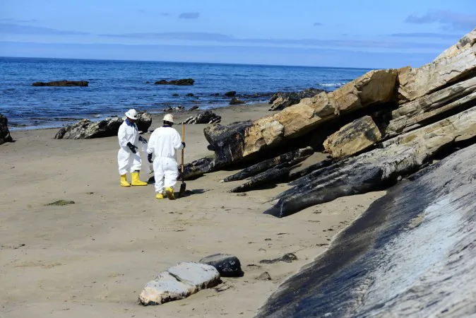 In this Saturday, May 23, 2015 photo released by the U.S. Coast Guard, two cleanup crew members work to remove oil from the sand along a portion of soiled coastline near Refugio State Beach, north of Goleta, Calif. (Chief Petty Officer David Mosley/U.S. Coast Guard via AP)