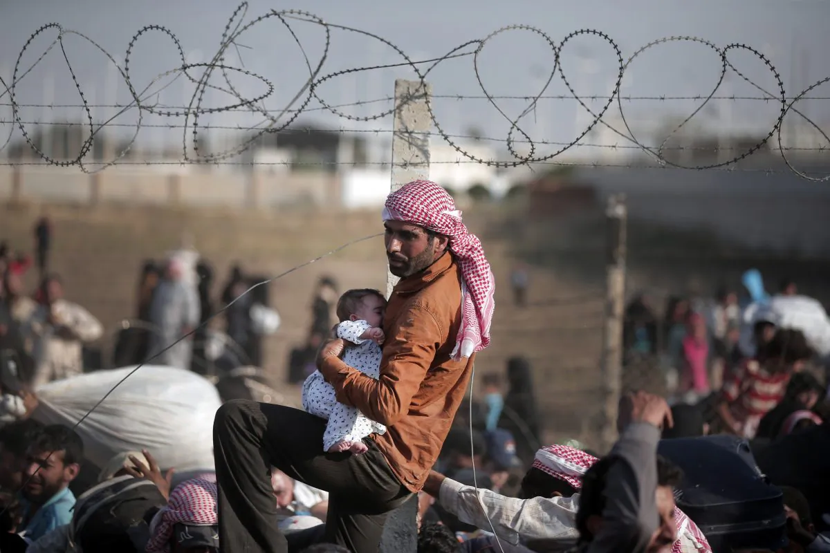 A Syrian refugee carries a baby over the broken border fence into Turkey after breaking the border fence and crossing from Syria in Akcakale, Sanliurfa province, southeastern Turkey, on Sunday. (AP Photo/Lefteris Pitarakis)