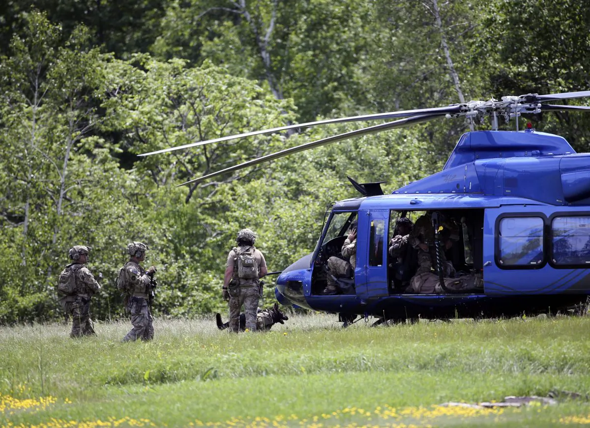 Law enforcement officers walk to a waiting helicopter after searching a wooded area near the Saranac River on Sunday, June 14, 2015, in Saranac, N.Y. (AP Photo/Mike Groll)