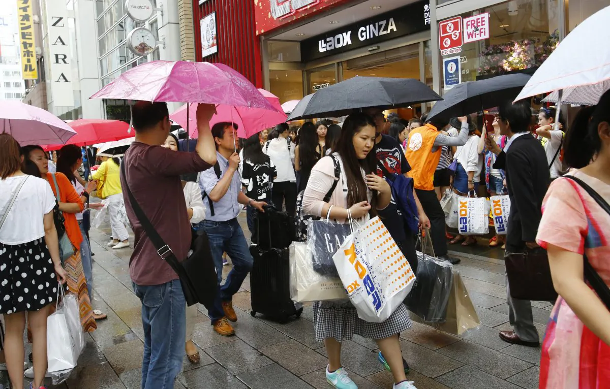 In this June 17, 2015 photo, Chinese tourists with shopping bags wait for a sightseeing bus in front of a discount electronics store in Tokyo's Ginza district.  (AP Photo/Shizuo Kambayashi)