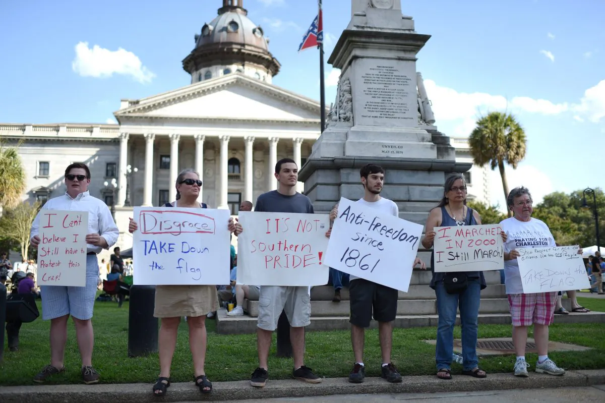 Protesters hold signs in front of the Confederate flag during a rally to take down the flag at the South Carolina Statehouse, Saturday, June 20, 2015, in Columbia, S.C.  (AP Photo/Rainier Ehrhardt)