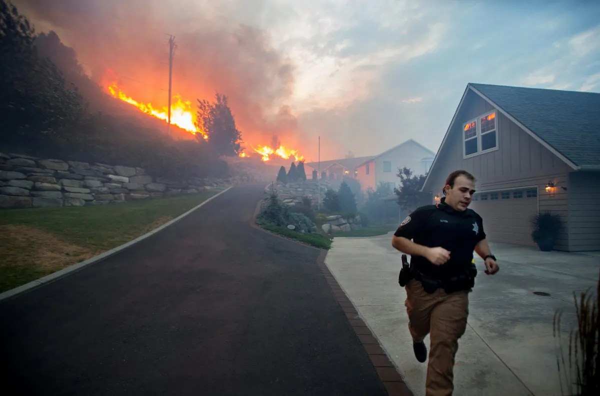 A Chelan County Sheriff's deputy races to check that all residents have left their home as flames approach houses at Quail Hollow Lane in Wenatchee, Wash. (Don Seabrook/The Wenatchee World via AP)