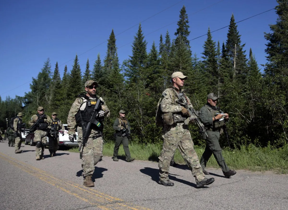 In this Wednesday, June 24, 2015 photo, Law enforcement officers walk along a road before going into the woods near Mountain View, N.Y. (AP Photo/Mike Grol)