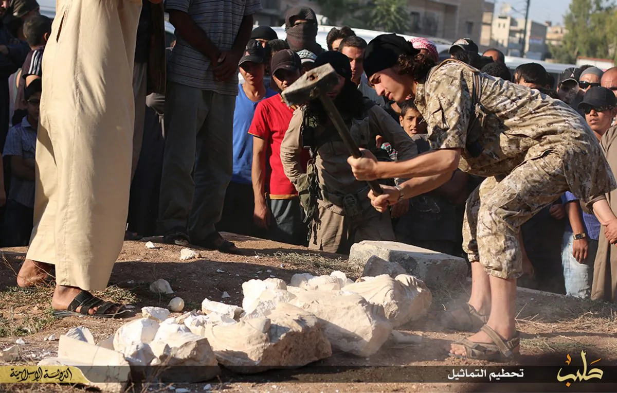 In this image posted on a militant website by the Aleppo branch of the Islamic State group on Friday, July 3, 2015, which has been verified and is consistent with other AP reporting, a militant smashes items that the group claims are smuggled archaeological pieces from the historic central town of Palmyra, Syria. (Militant website via AP)