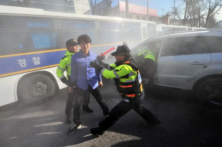 Policemen arrest a South Korean driver (C) walking out of his vehicle after repeatedly crashing into a police bus shielding the Chinese embassy in Seoul on Dec. 13, 2011 while activists stage a protest outside the embassy to denounce Beijing for the killing of a South Korean coastguard officer by a Chinese fishing boat captain. (Jung Yeon-Je/AFP/Getty Images)
