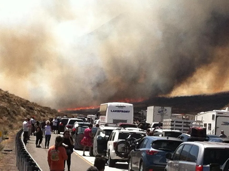 Bystanders look on along Interstate 15 on the Cajon Pass, Friday, July 17, 2015, near San Bernadino, Calif., as a fast-moving wildfire swept across the Southern California freeway, destroying numerous vehicles and sending motorists running to safety before burning at least five homes. (Arsenio Alcantar via AP)