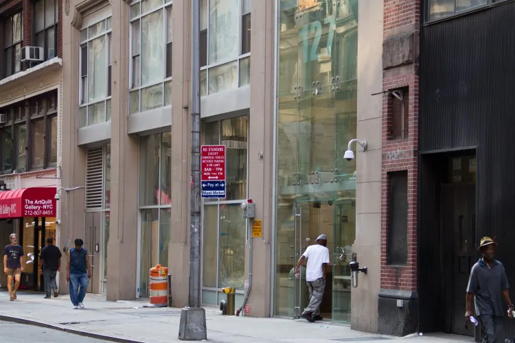People walk by the store of the City Quilter as a woman on her cellphone rests on a fire hydrant in Chelsea area of Manhattan on June 16. Dale Riehl, the store owner, said that customers don't like to come in when people are sitting on the hydrants. (Benjamin Chasteen/The Epoch Times)