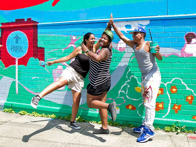 (L-R) Ayhn Gonzalez, Tamika McLean, and Yoiky Brito, do a team "high five" before they start painting the mural on the wall of a nonprofit organization, Rocking the Boat, located in Bronx, N.Y., on Aug. 13. The team has been painting the mural since July. (Benjamin Chasteen/Epoch Times)